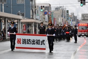 出初式の看板を持ち、行進する消防署員の画像