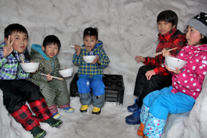 大きなかまくらの中で餅を食べる子どもの画像