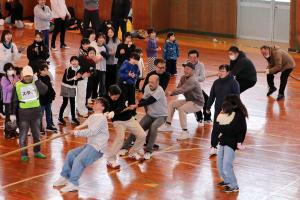 子どもたちの声援を受けながら綱引きをする男性の画像