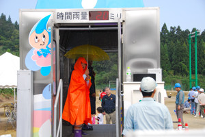 降雨体験車で大雨体験をする子どもの画像