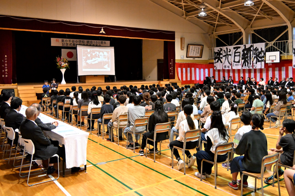 東小千谷小学校の歩みを朗読する児童とそれを聞く全校児童・来賓の画像