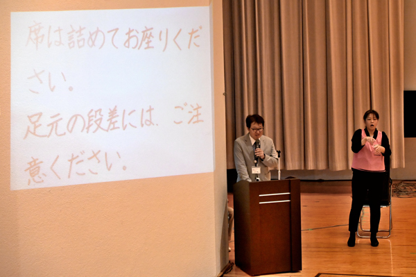 司会進行に合わせて手話通訳と要約筆記がされている様子